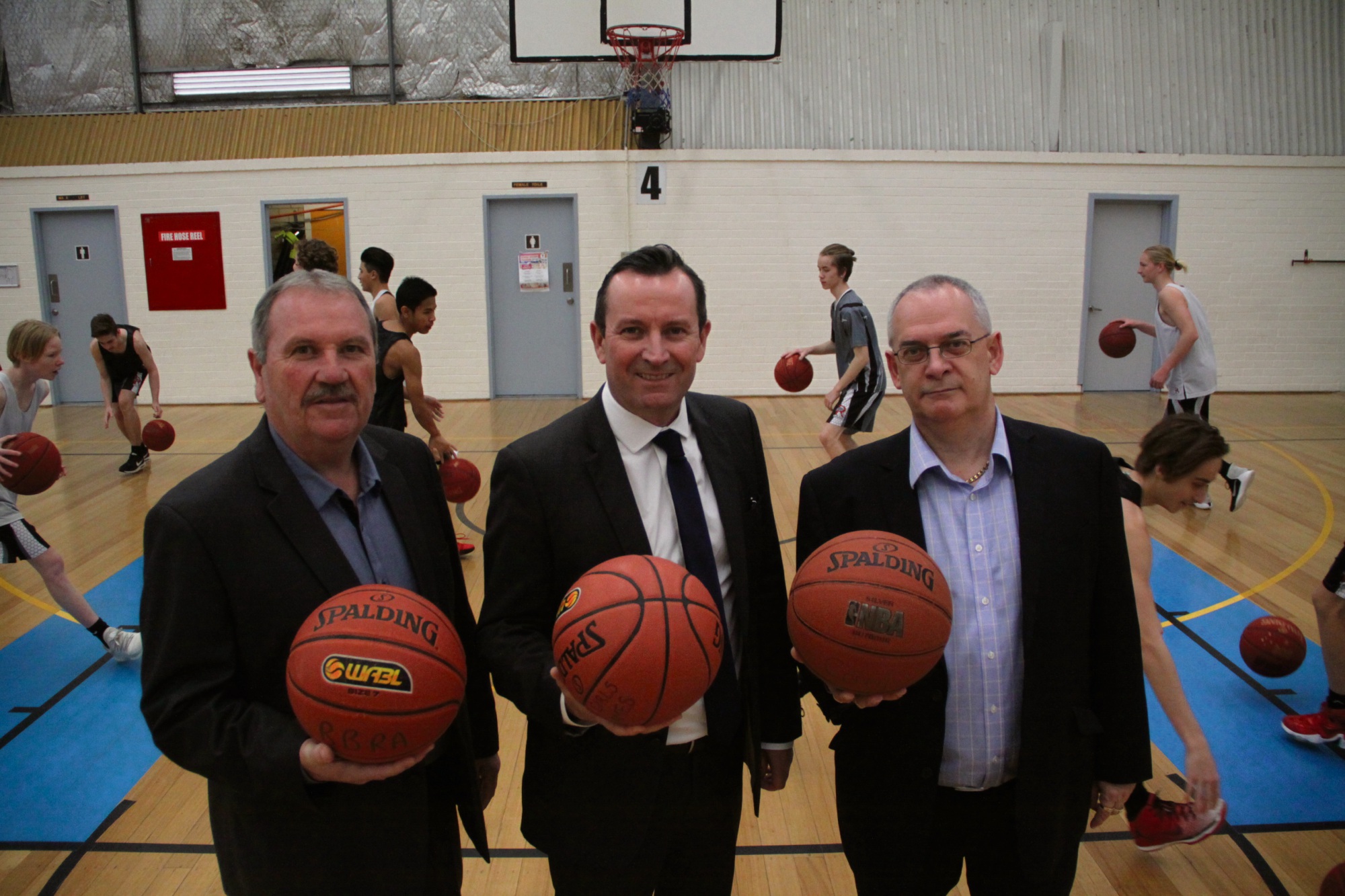 Mayor Barry Sammels, Premier Mark McGowan and Rockingham Flames President Clive Higgins in front of Rockingham High School students at a training session.