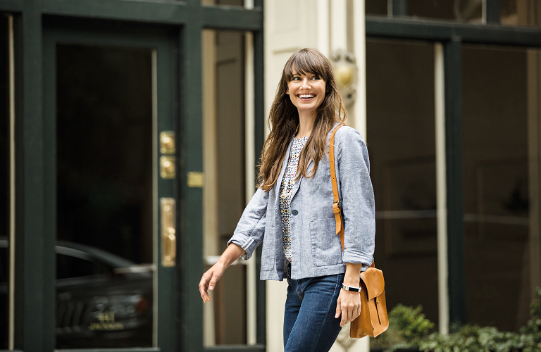 A woman wearing a Fitbit Alta and smiling brightly as she walks.