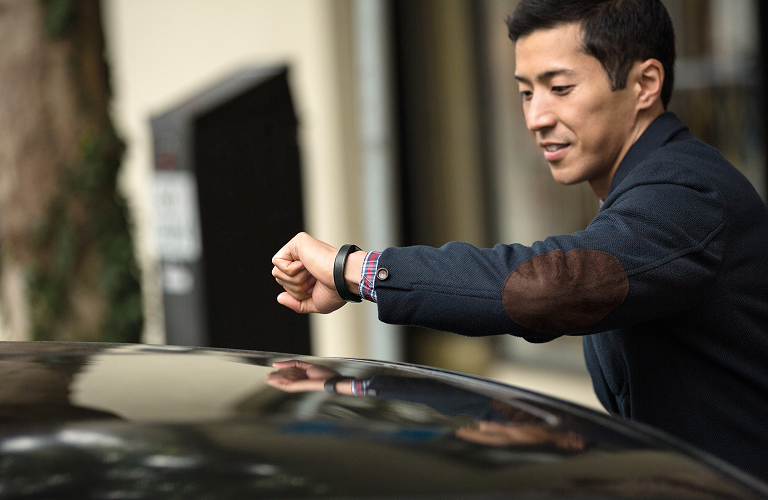 A man checking his Fitbit Alta as he gets into his car.