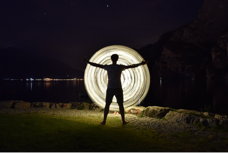 A nighttime photo of a man standing in front of a wheel of light