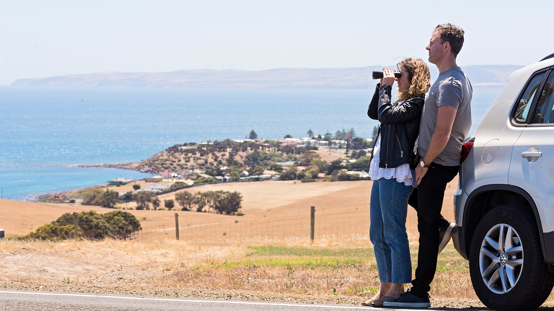 couple looking at penneshaw through binoculars while leaning against their grey car