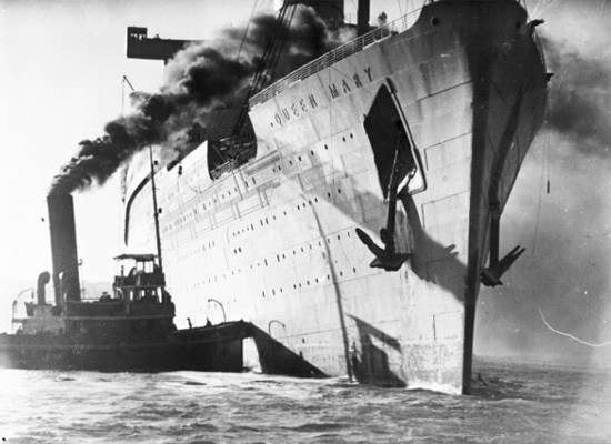 Black and white photograph of Queen Mary troopship with tug boat alongside