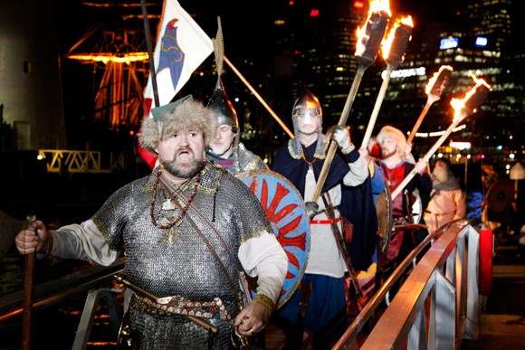 Group of people dressed as Vikings walk up ramp, holding fire torches