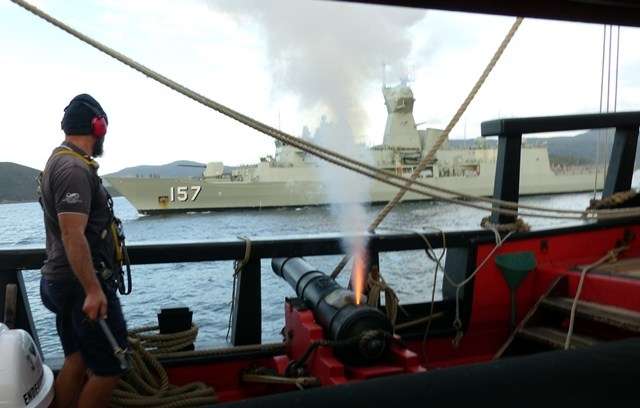 Gunner Cody Horgan firing the cannon on Endeavour, with HMAS Perth in the background