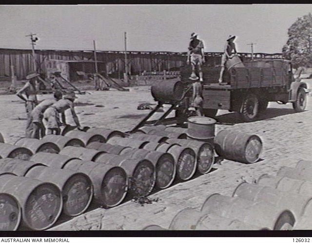 1946-02-26. MEN ROLLING DRUMS OF RANGE FUEL TOWARDS A MECHANICAL LOADER ...