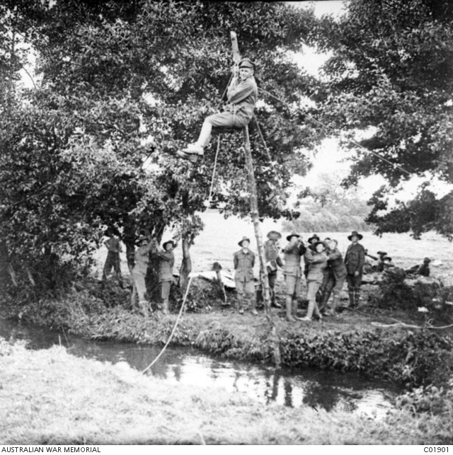 Members of the 61st Battalion hoist one of their comrades over a river ...