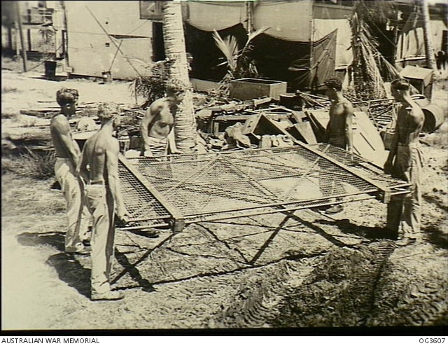 LABUAN, NORTH BORNEO. 1945-10-18. RAAF AIRMEN CARRYING A DISMANTLED ...