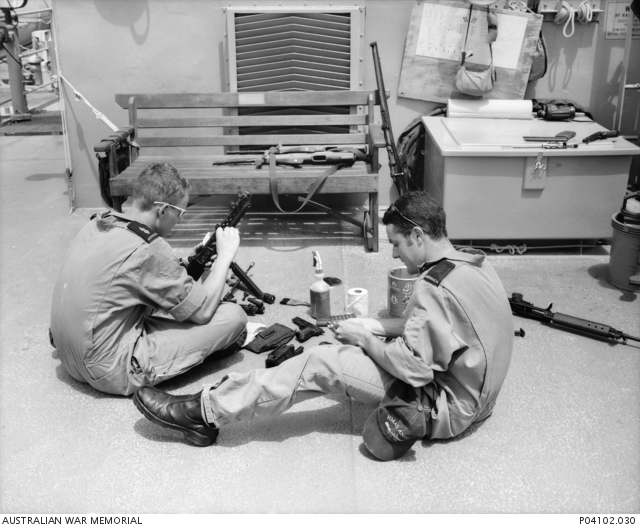 Two unidentified crew members clean and check their weapons on the gun