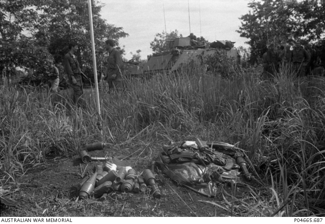 A pile of captured enemy weapons and ammunition lie on the ground ...