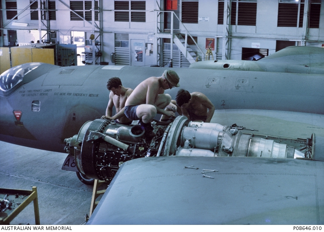 Three engine fitters straddle the engine of an RAAF 2 Squadron Canberra ...