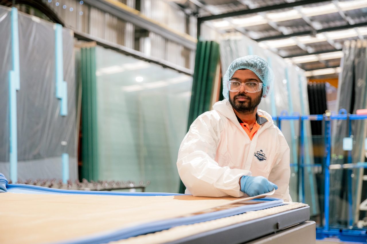 Lamination technician working beside stacked glass panels in the Tough Glass facility.