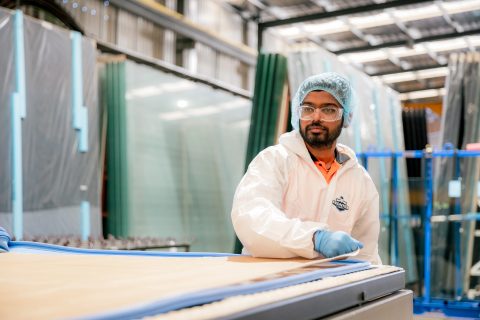Lamination technician working beside stacked glass panels in the Tough Glass facility.