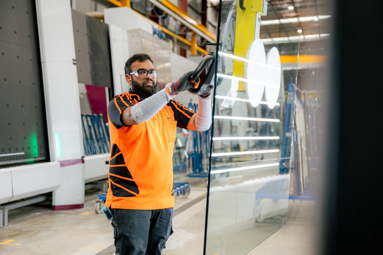 Tough Glass operator moving a large glass panel with a suction lifter.