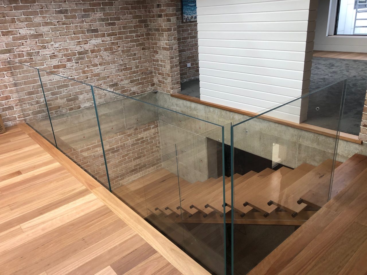 Frameless glass balustrade surrounding a timber staircase and upper landing.