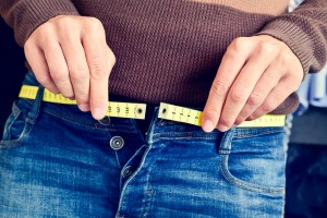 a young man measuring his waist as jeans buttons are unfastened