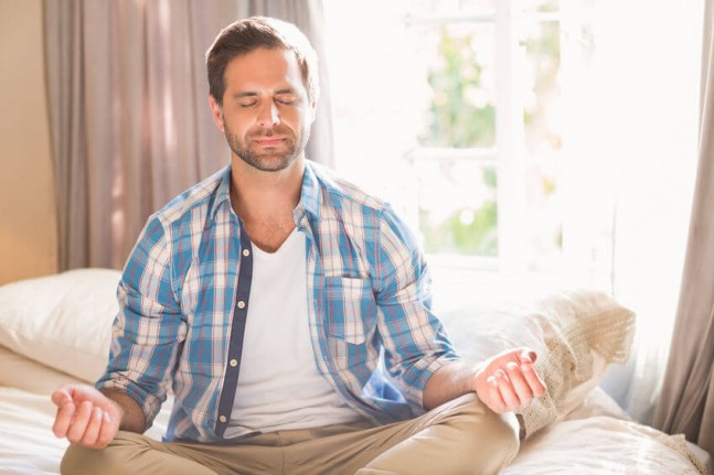 Handsome man practising meditation on his bed at home in bedroom
