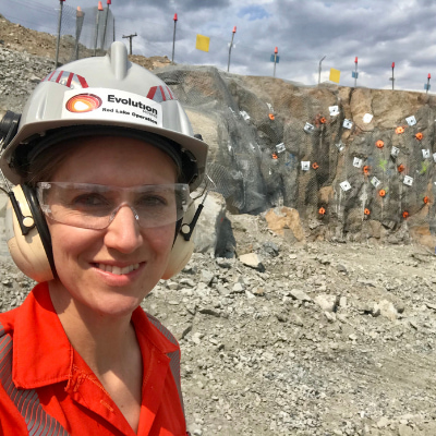 White woman in hard hat, safety goggles and ear defenders, standing in a quarry