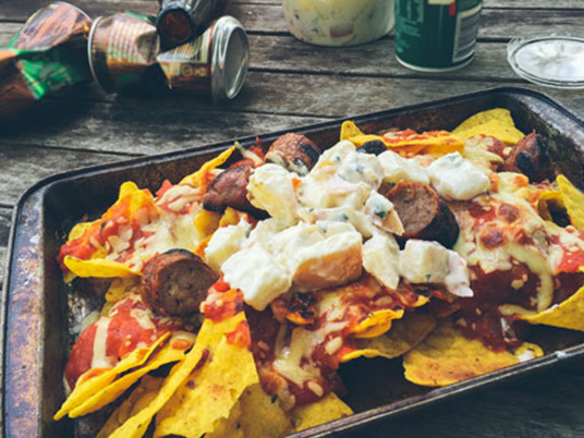Nachos laying in an oven dish with some empty cans laying behind it
