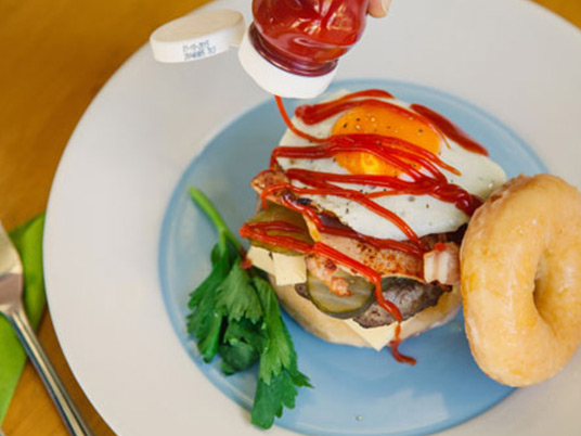 A donut burger with and individual pouring tomato sauce over it