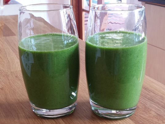 Two glasses next to each other with a green smoothie liquid in them