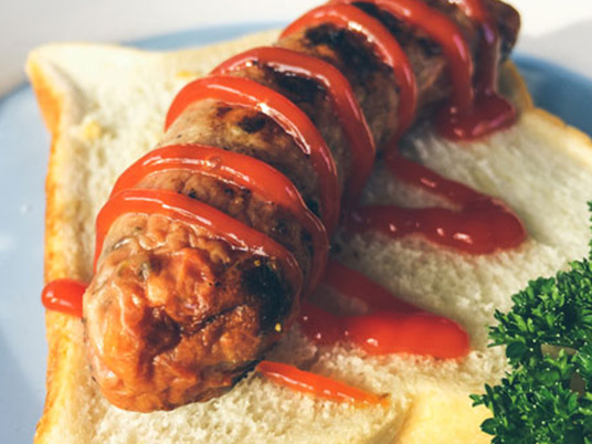A sausage laying on a white piece of bread with tomato sauce on top
