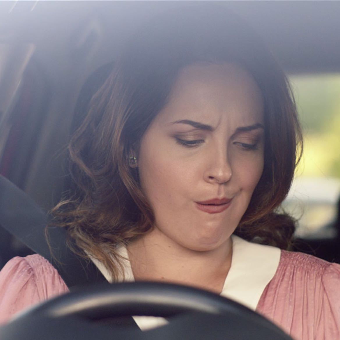 Close up shot of woman sitting in car and pulling a funny face looking down at the centre console