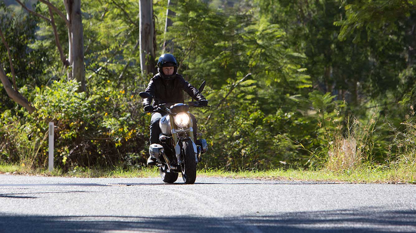 View of BMW motorcycle rider with open face helmet driving on road towards camera