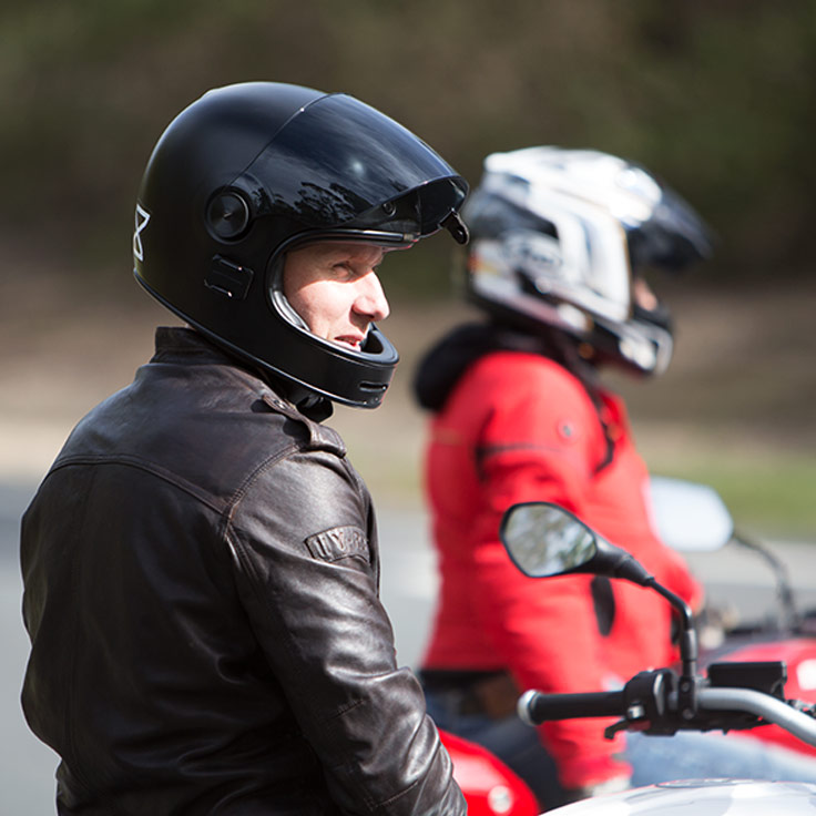 View of male motorcycle rider with open face helmet parked and staring off into the distance