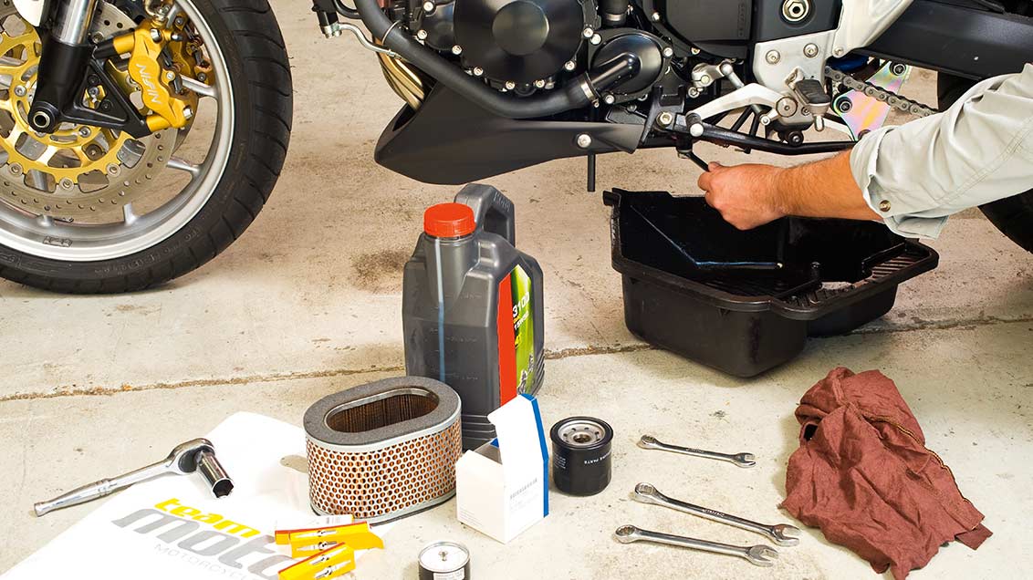 Lower view of motorcycle having an oil change with various tools laying on the floor near it