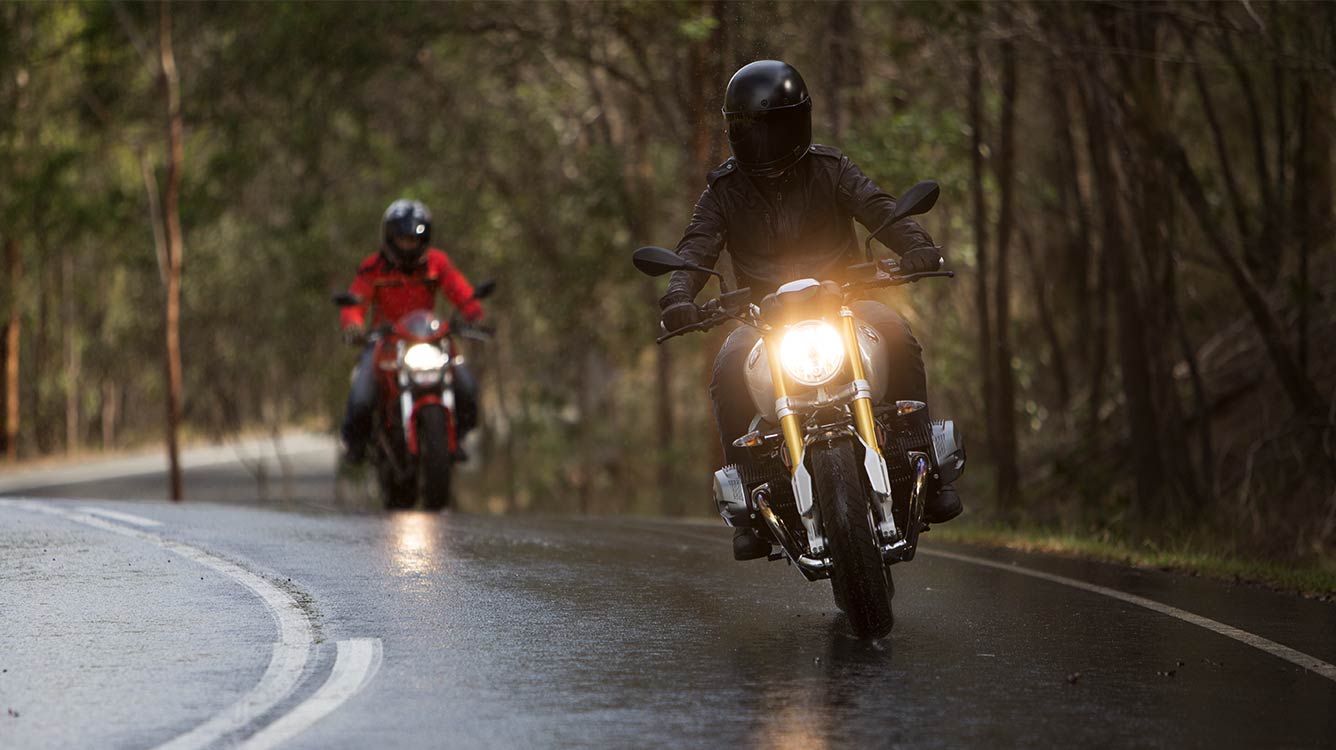 View of two motorcyle riders moving towards camera on a wet road surface