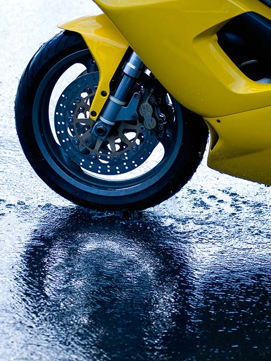 View of front tyre of yellow sports bike on a wet road surface