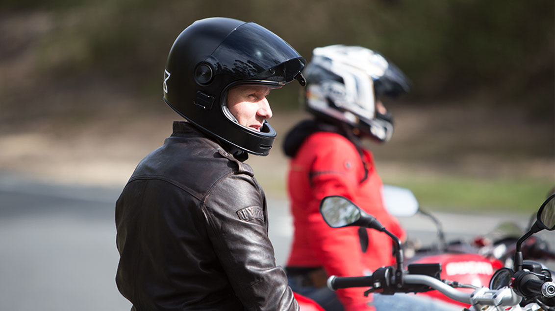 View of male motorcycle rider with open face helmet parked and staring off into the distance