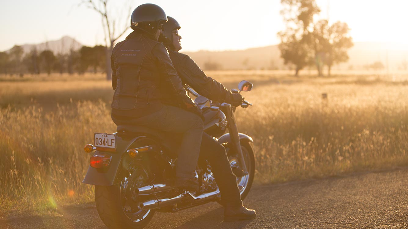A man and a women sitting on a cruiser motorcycles looking at the sunset