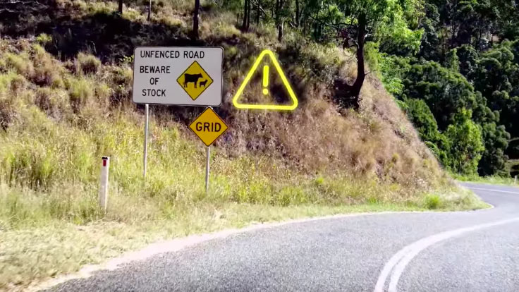 View of winding road with warning sign mentioning cattle grids and live stock up ahead
