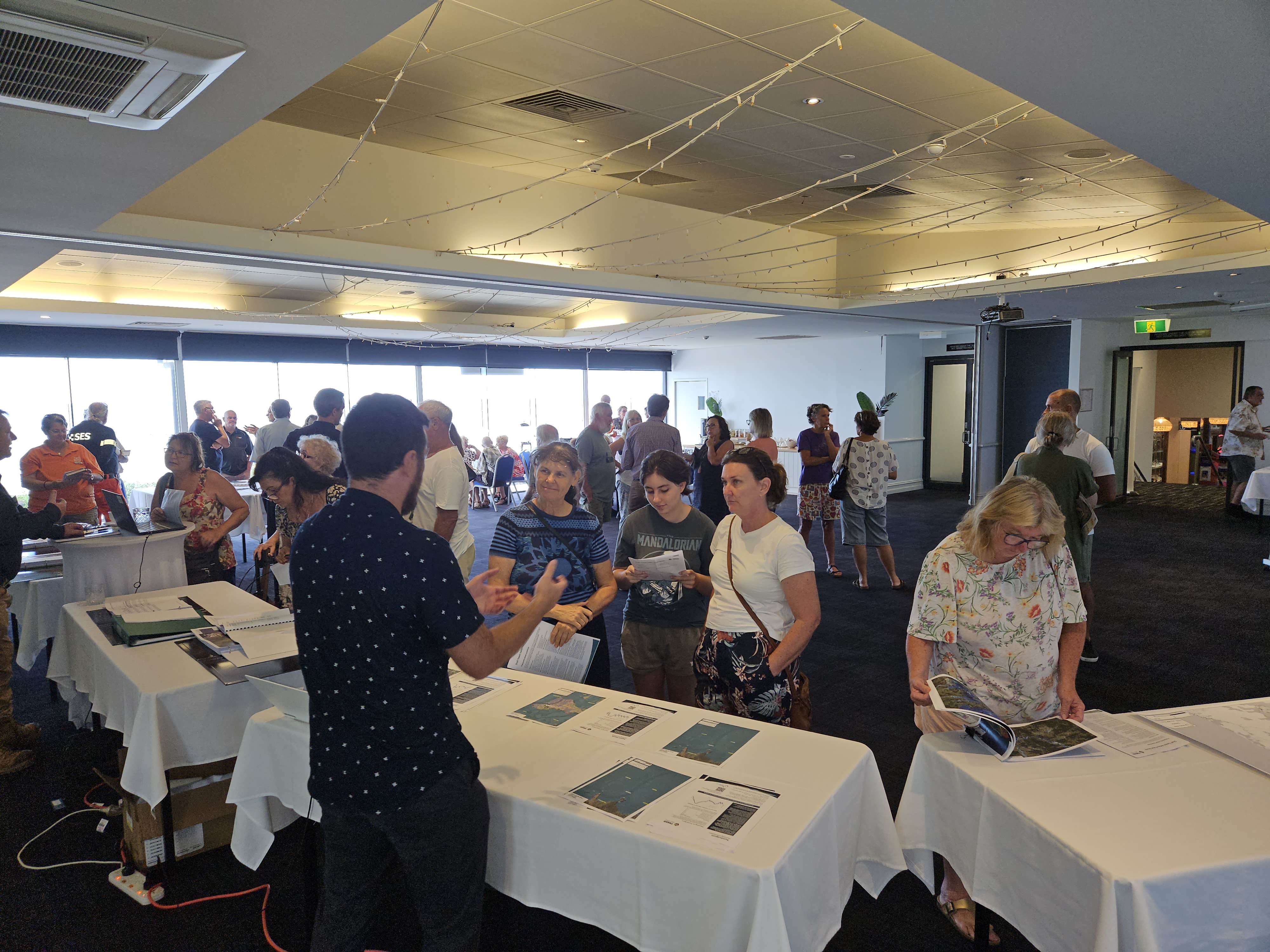 Indoor community consultation event with several tables displaying planning documents and maps, where attendees are speaking with Council staff and reviewing printed materials.