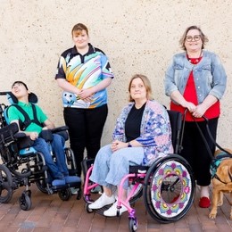 four people in a groups different ages and gender, two standing and two in wheelchair one electric one manual