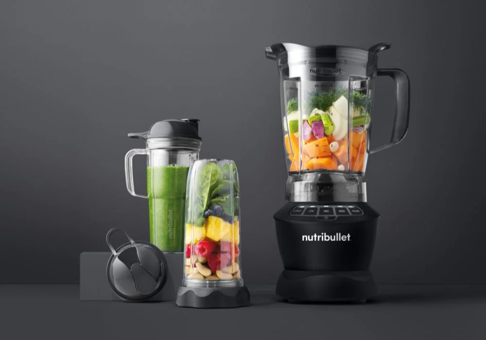 A Nutribullet full-sized blender on a kitchen counter with fresh ingredients around it.
