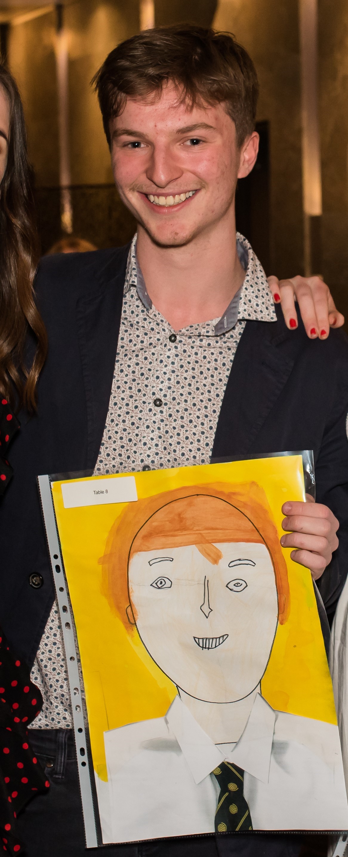Davis Evans at the IGS graduation dinner with a portrait of him painted by a Year 1 student