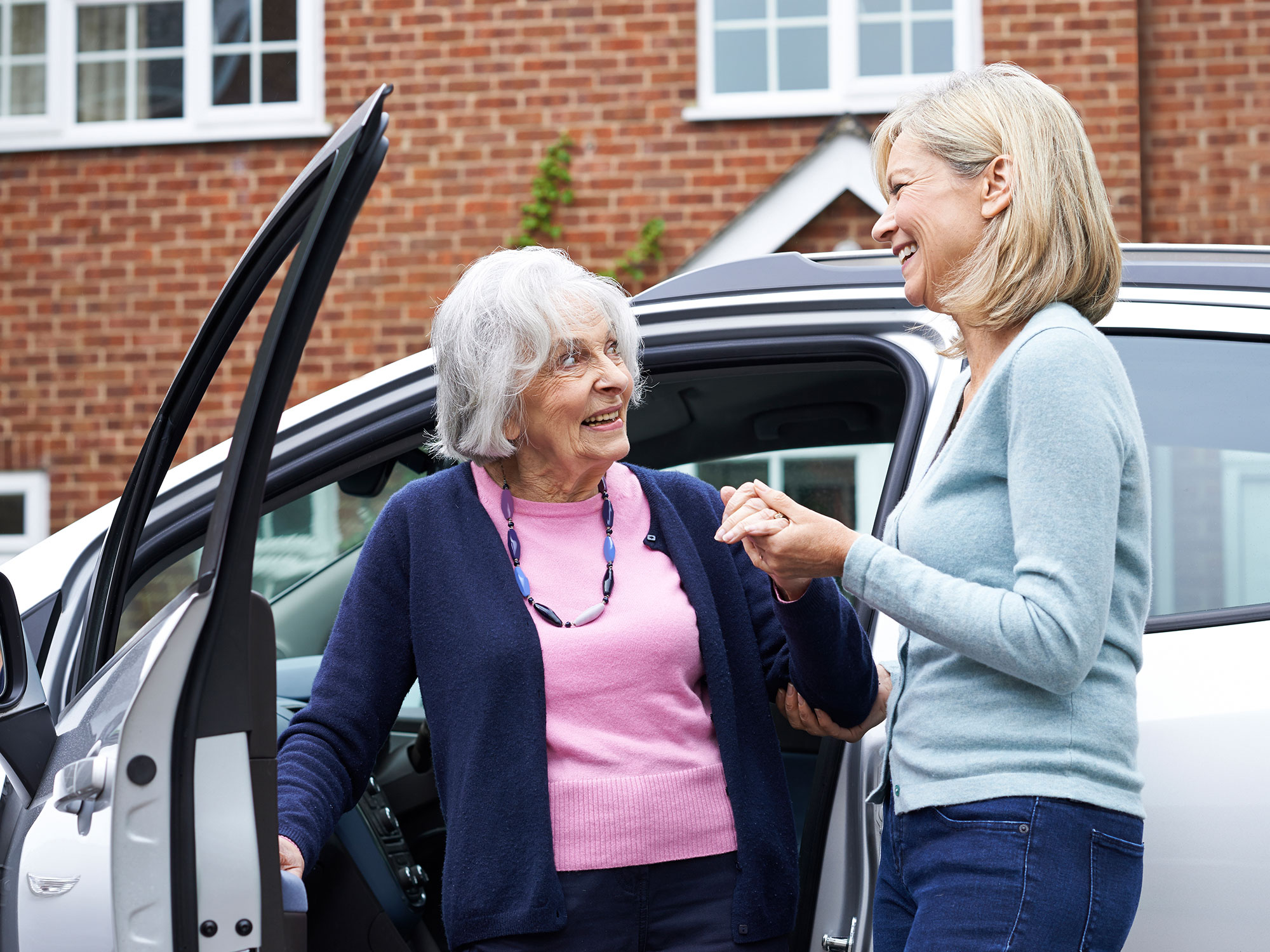 A carer helping an older woman get out the car.