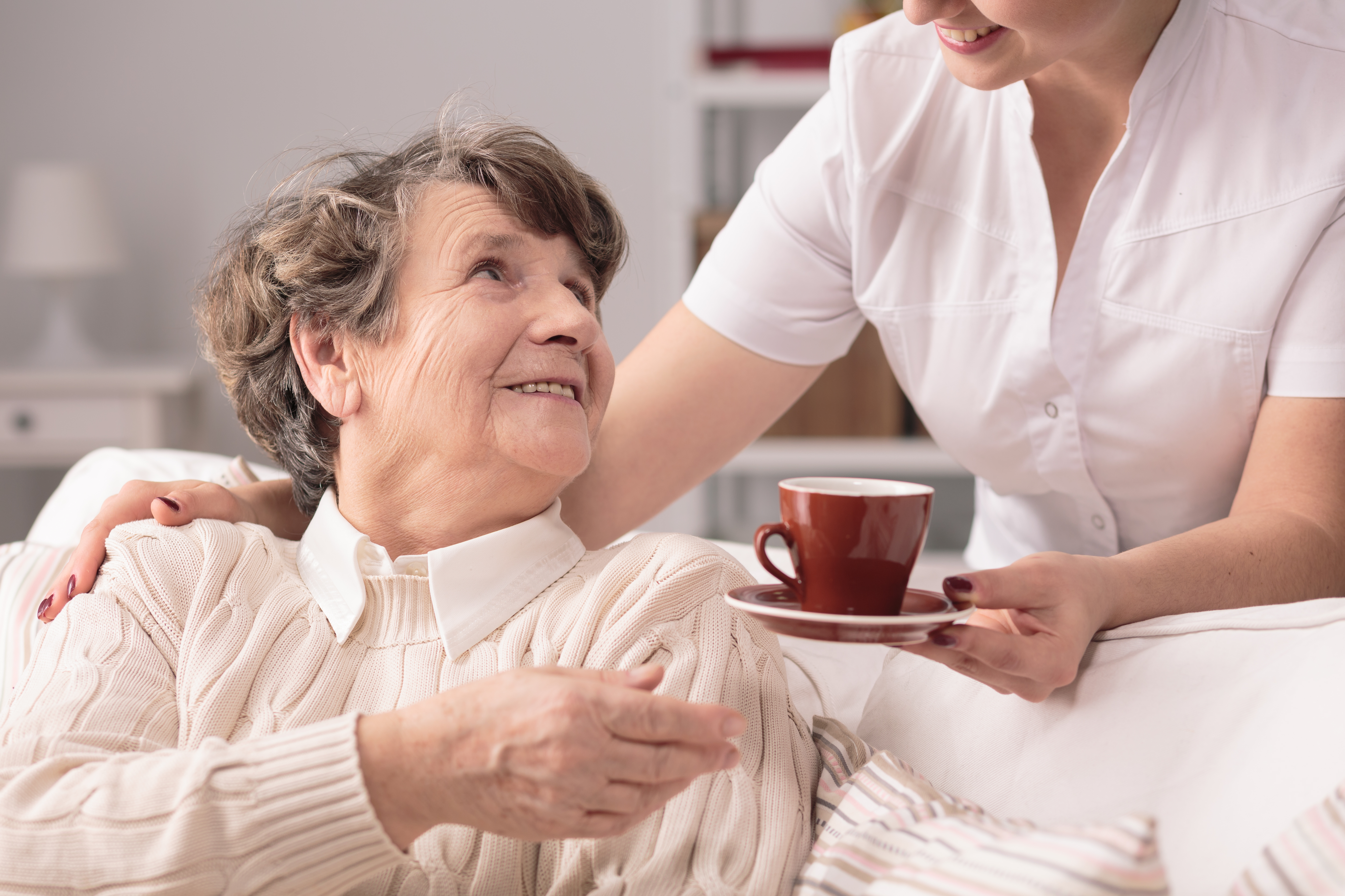 Older woman accepting tea from a carer at her home.