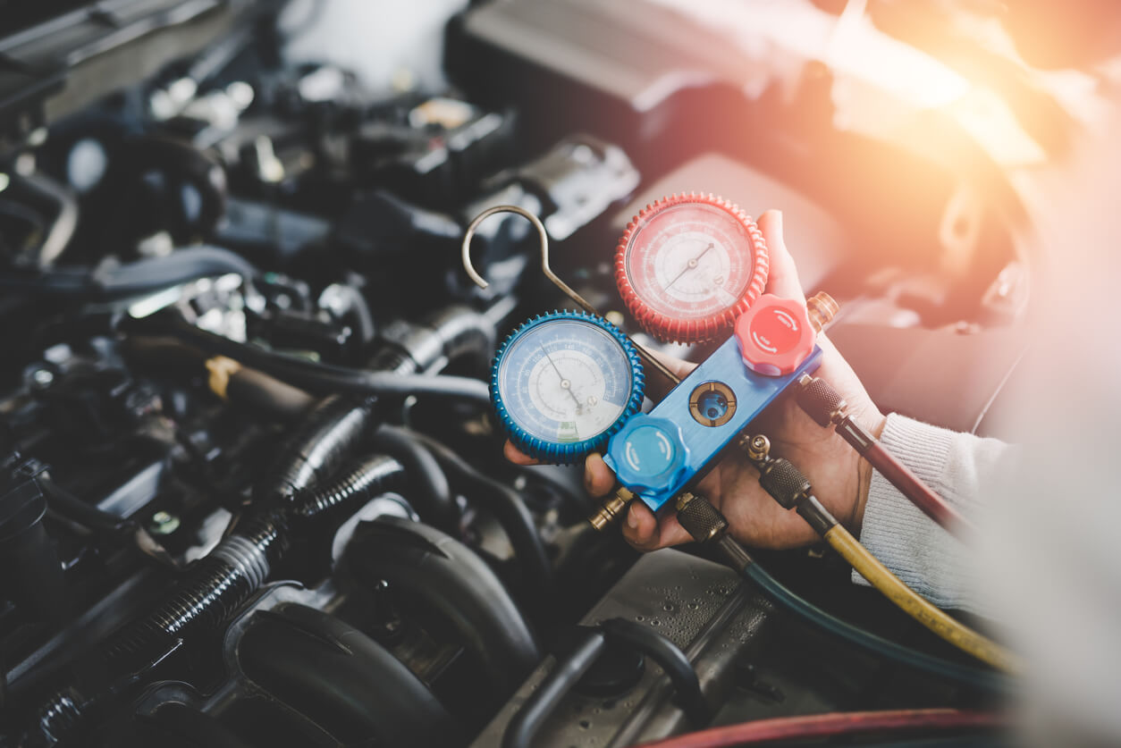 Recharging and servicing Air conditioning Technician using pressure tools to flush and refill air conditioning system in car
