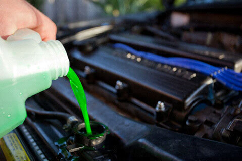 Hand pouring green coolant into a car radiator with the engine exposed