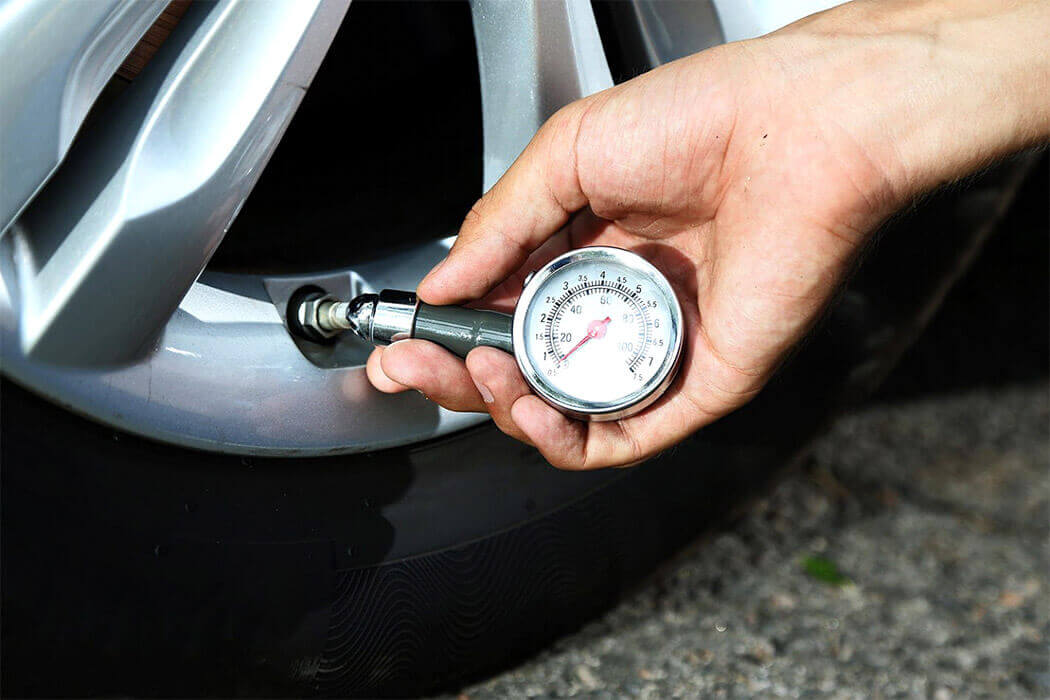 Hand using a tyre pressure gauge to check the air pressure of a car tyre valve