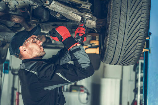 The main purpose of the suspension system in your car is to keep all of the tyres firmly attached to the ground. Caucasian car mechanic adjusting tension in vehicle suspension element.