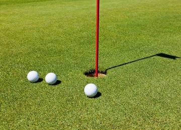 Three golf balls on the putting green, next to the hole