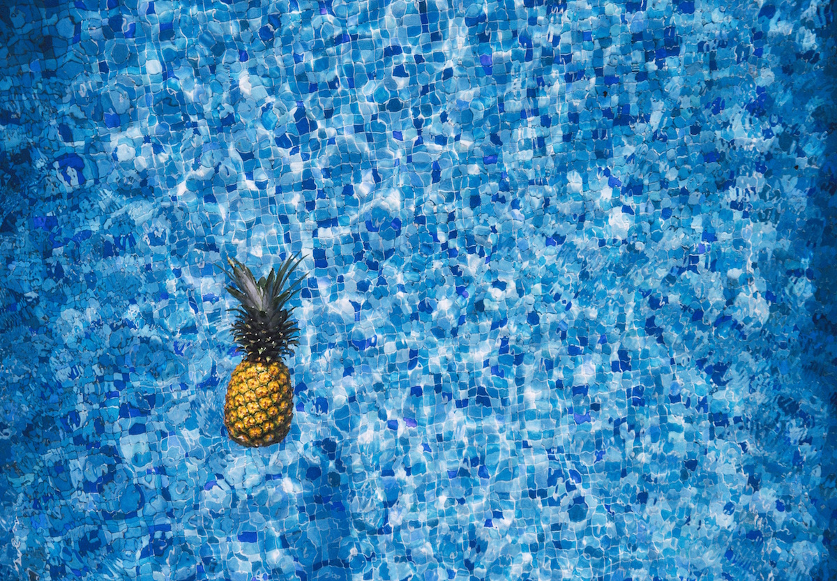 A pineapple floats in a bright blue swimming pool.