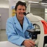 Dr Cathy Gorrie wearing a lab coat and using a microscope