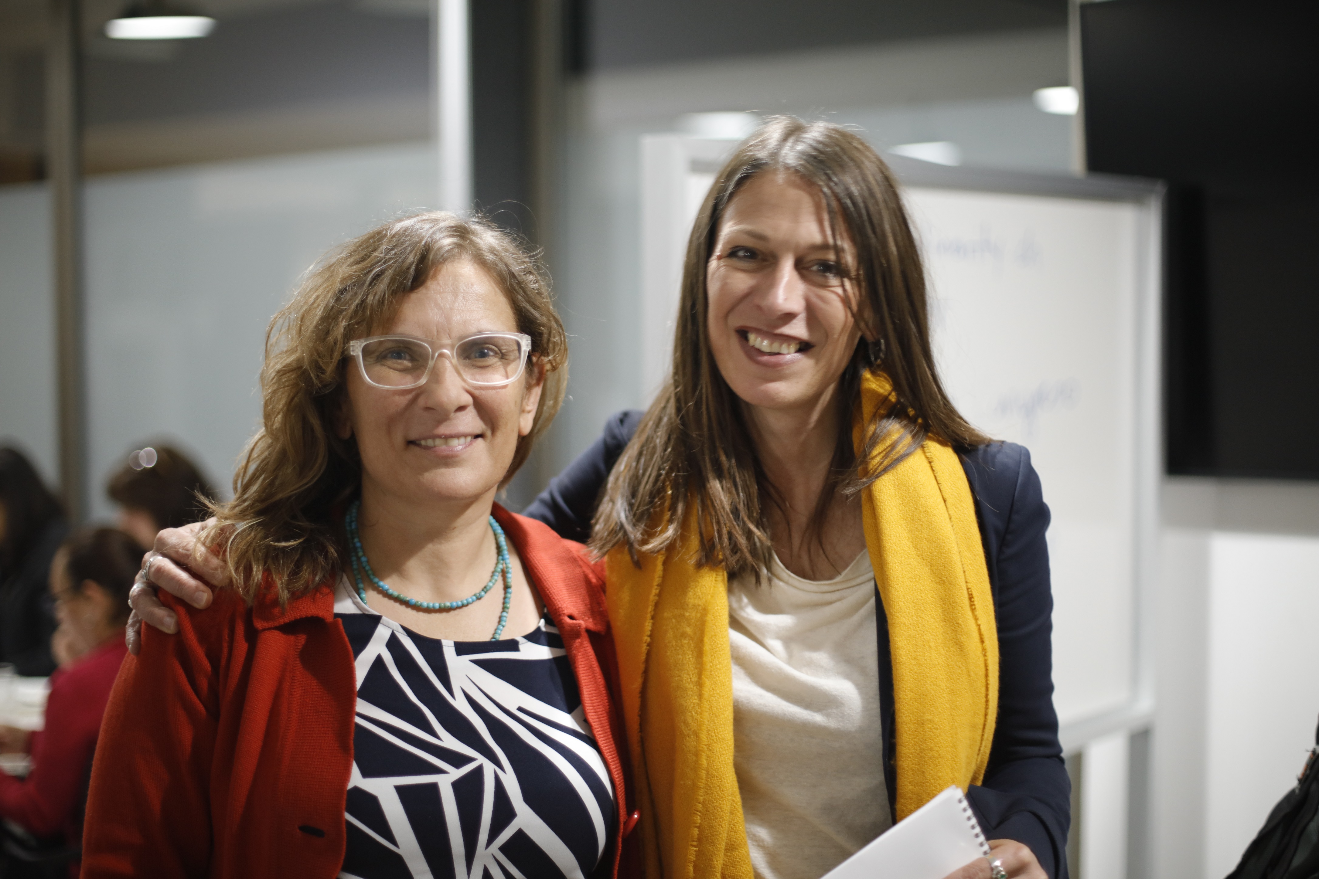Two women standing in an office embracing for the camera