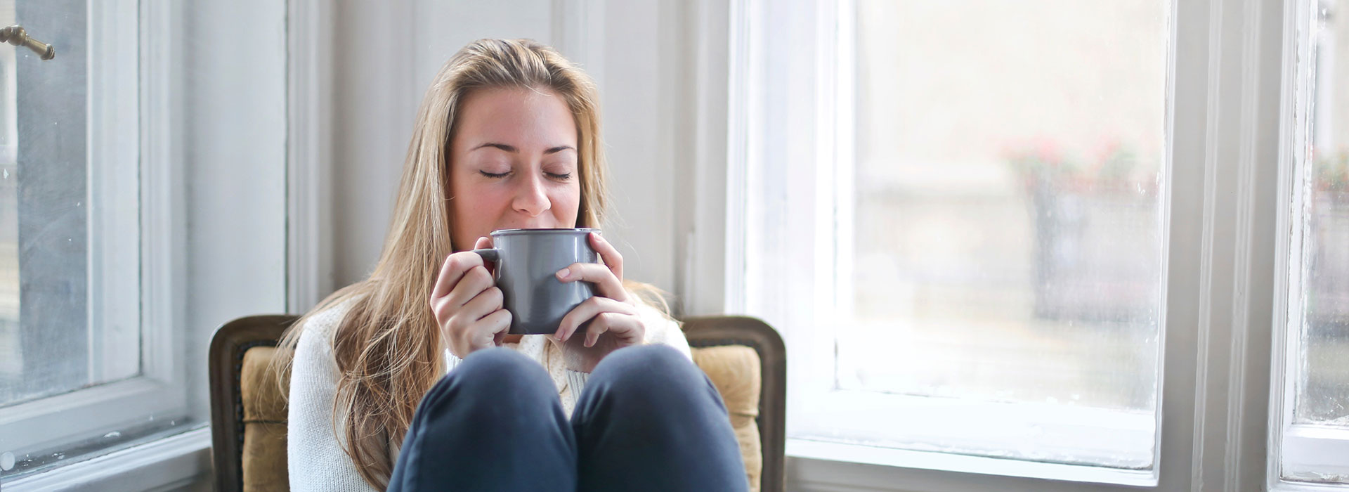 A blonde woman sitting on a lounge drinking tea.
