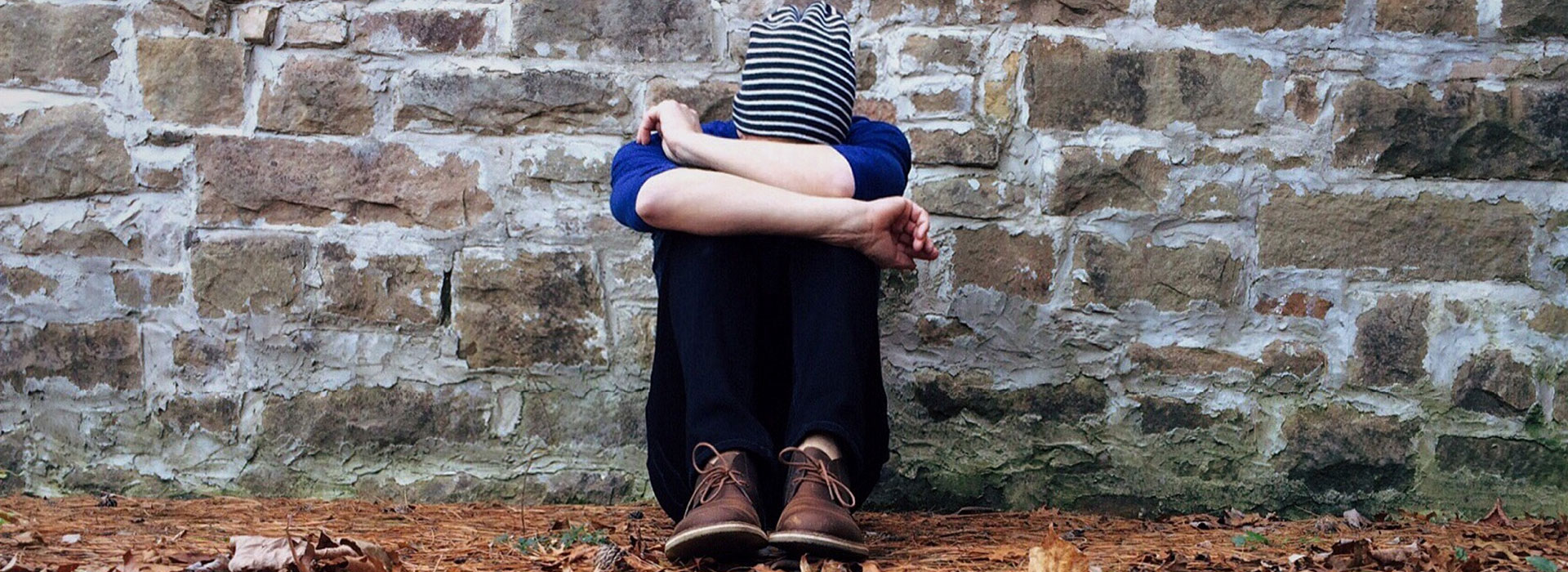 A young man wearing a striped beanie with his head in his lap.